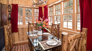 Un intérieur en bois avec une table à manger pour quatre personnes, de grandes fenêtres et un lustre.