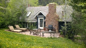 Un chalet rustique avec une cheminée en pierre, une terrasse dotée de mobilier d’extérieur et une porte avec une fenêtre.
