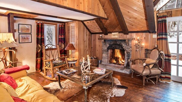 L’int érieur d’un chalet confortable, avec des murs en rondins de bois, une cheminée en pierre, des meubles en bois et une grande fenêtre agrémentée de rideaux.