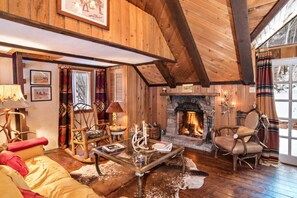 A cozy log cabin interior with a stone fireplace, wooden furniture, and a large window with curtains. - Historic Cottage on Private Estate, Pool & Tennis, Dog Friendly! (Redstone)