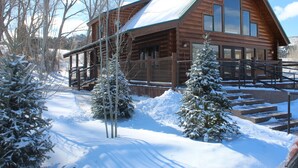 A log cabin with a covered porch, snow-covered trees, and steps leading to the entrance. - Beautiful Newly Remodeled Log Cabin at Tiny Timbers Resort! (South Fork)