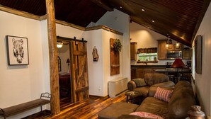 A cozy living room with a sectional sofa, wooden flooring, and a rustic kitchen in the background. - Beautiful Newly Remodeled Log Cabin at Tiny Timbers Resort! (South Fork)