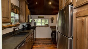 A kitchen with wooden cabinets, a stainless steel refrigerator, and a window with a view of greenery. - Beautiful Newly Remodeled Log Cabin at Tiny Timbers Resort! (South Fork)