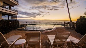 Ein Pool direkt am Strand mit Liegestühlen, einer Palme und Blick auf den Sonnenuntergang.