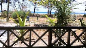 A view from a covered outdoor area with a wooden fence, overlooking a beach with trees and a clear sky. - Hotel Gili Air & Restaurant (Gili Air)