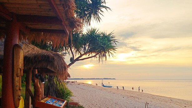 A beach with a thatched-roof structure, a calm sea, and a sunset. - Hotel Gili Air & Restaurant (Gili Air)