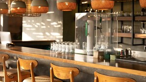 Zona de bar con sillas de madera, lámparas colgantes y una barra con vasos y botellas.