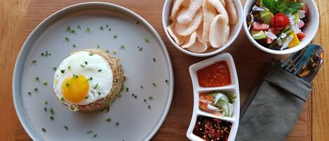 A breakfast plate with a fried egg on toast, a bowl of chips, a fruit salad, and two dipping sauces on a wooden table.