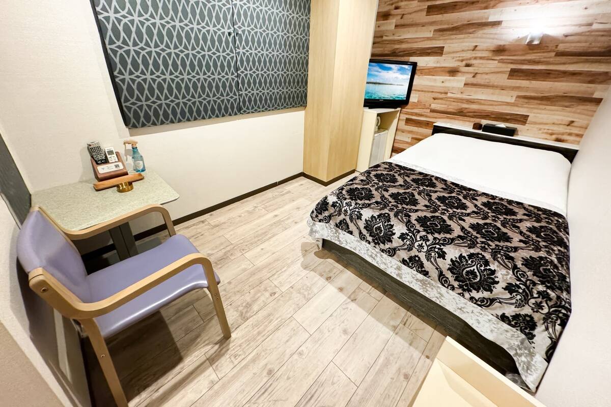 Une chambre d’hôtel avec un lit, un bureau et une chaise, un téléviseur fixé au mur et une couvre-lit à motifs.