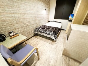 Une chambre d’hôtel de taille réduite, comprenant un lit, un petit bureau, une chaise et un téléviseur.