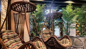 Wicker stoelen met gestreepte kussens in een ruimte met een stenen muur en tropische planten.