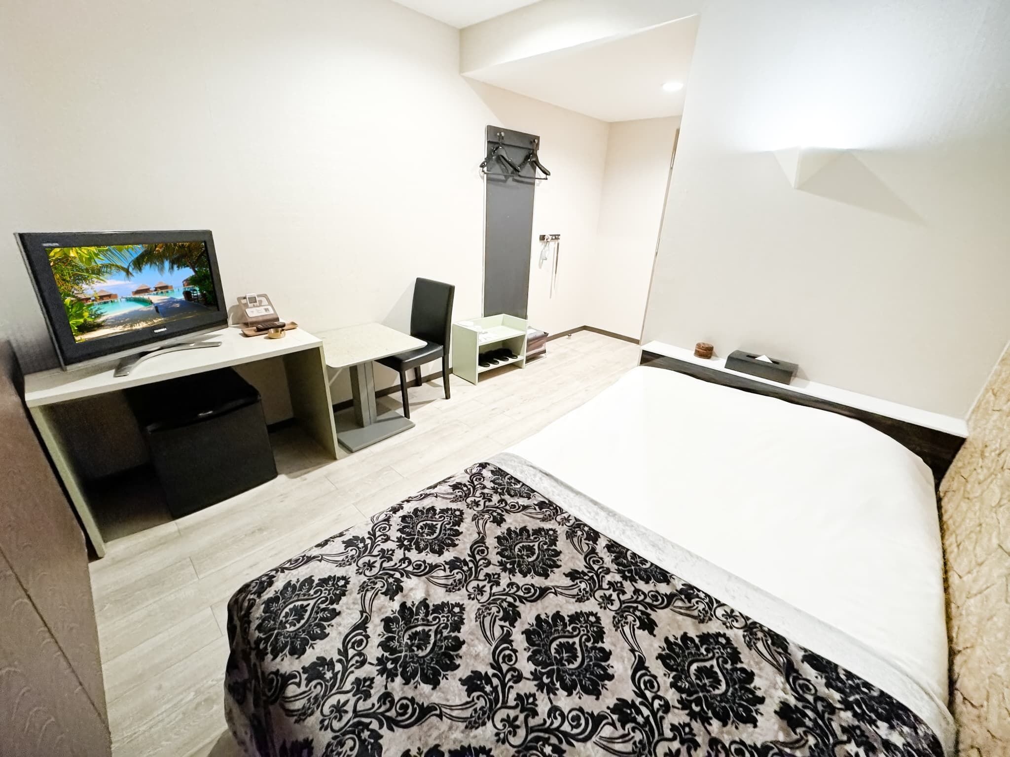 Una habitación de hotel con una cama, un escritorio con televisor, una silla y un estante pequeño.
