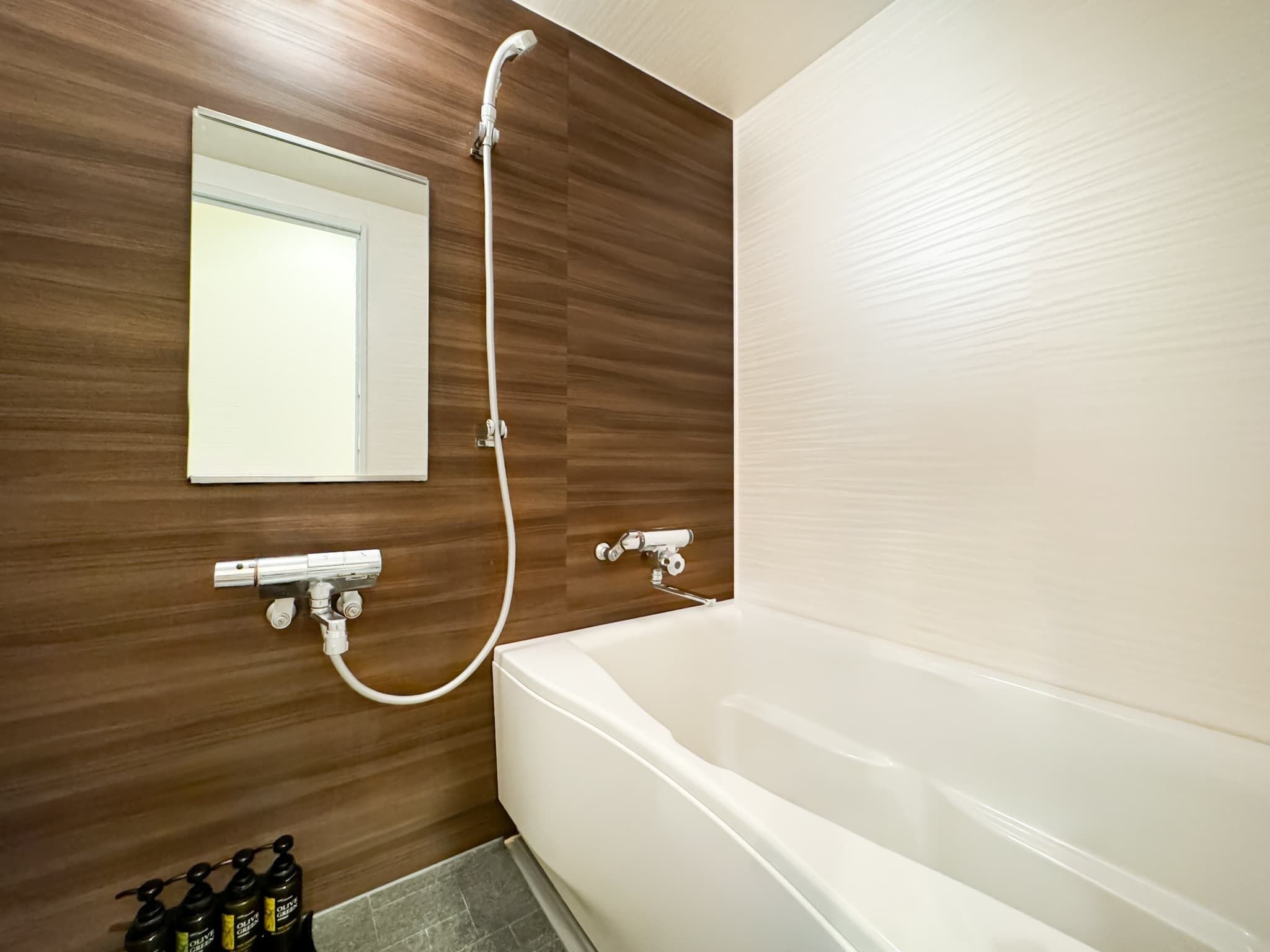 Un baño moderno con pared de madera, una bañera blanca, un cabezal de ducha manual y un espejo.