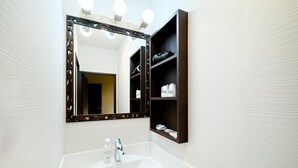 Ein Badezimmer mit weißem Waschbecken, einem beleuchteten Spiegel und einem Ablagefach für Toilettenartikel.