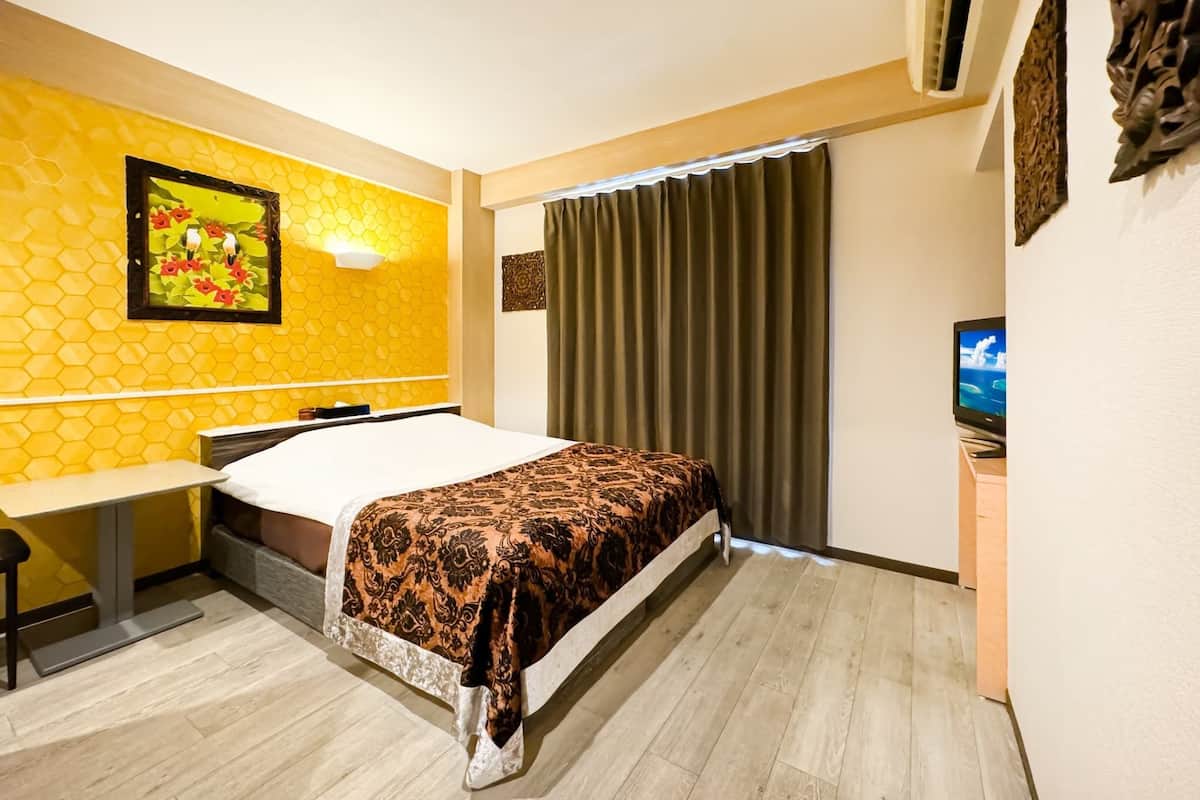 Une chambre d’hôtel équipée d’un lit, d’un bureau, d’une chaise, d’une télévision et d’une fenêtre avec des rideaux.