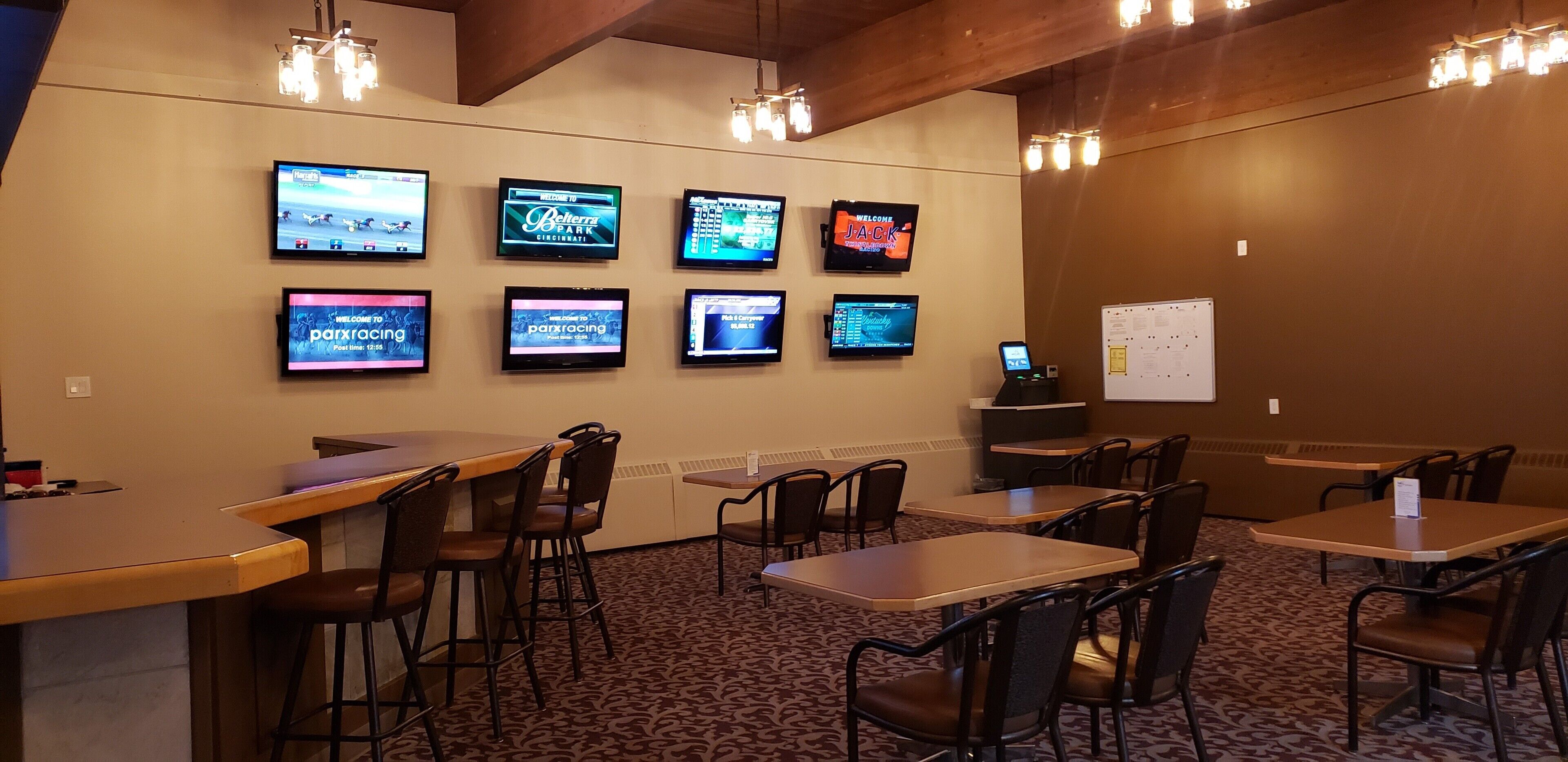 A conference room with multiple tables and chairs, a whiteboard, and several screens displaying racing events.