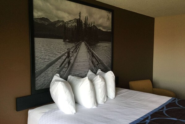 Ein Hotelzimmer mit einem Bett, einem großen gerahmten Bild einer Brücke über einem See und einem Sessel.