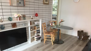 A living room with a TV, wooden chairs, a round table, and a bookshelf with books and decorative items. - Beachdoc, 300 m to the beach (St. Leonards)