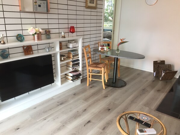 A living room with a TV, wooden chairs, a round table, and a bookshelf with books and decorative items.