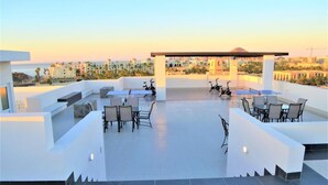 Une terrasse sur le toit avec des sièges extérieurs, un espace couvert et une vue sur le paysage urbain et la plage.