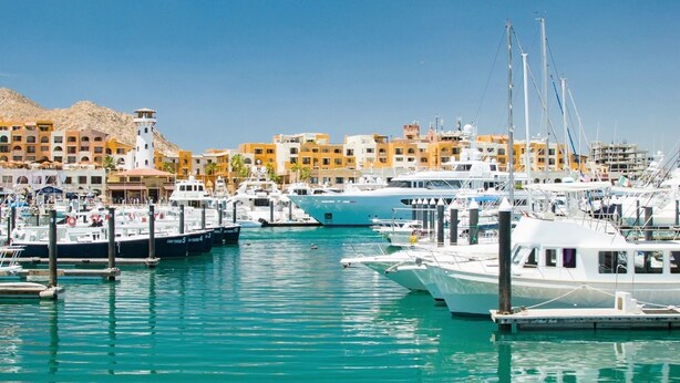 Un port de plaisance où sont amarrés différents types de bateaux, un ciel dégagé et des bâtiments en arrière-plan.