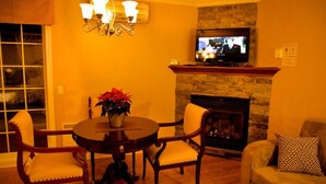 A cozy living room with a fireplace, a television mounted above it, a dining table with chairs, and a sofa with patterned cushions.