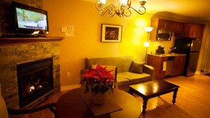 A living room with a fireplace, a television, a dining table with a vase of flowers, a sofa, and a kitchen area with cabinets and appliances.