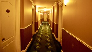 A hotel hallway with a carpeted floor, doors on both sides, and wall sconces providing light.