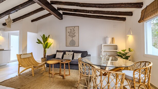 Una habitación con un sofá, dos sillones, una mesa de vidrio, una planta grande y una obra de arte colgada en la pared.