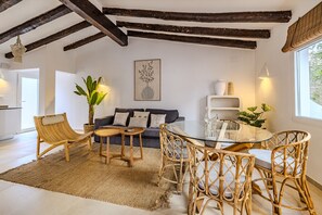 A room with a sofa, two chairs, a glass table, a large plant, and a wall-mounted artwork.