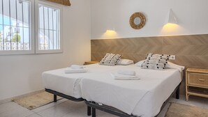 Un lit double avec du linge de lit blanc, deux tables de chevet, un luminaire fixé au mur et une fenêtre avec des stores.