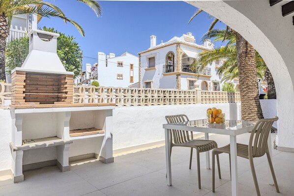 Un patio al aire libre con una parrilla, una mesa con sillas y vistas a edificios blancos con balcones.
