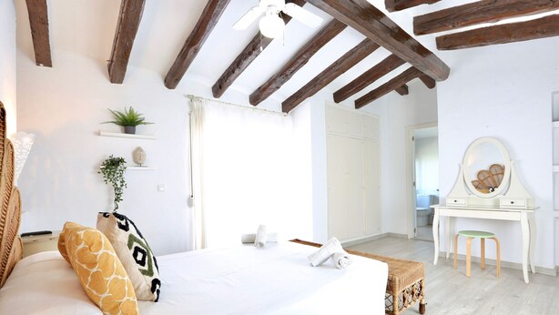 Ein Schlafzimmer mit einem Bett, einem Schreibtisch und einem Stuhl. Pflanzen stehen auf Regalen und ein Spiegel ist an der Wand.