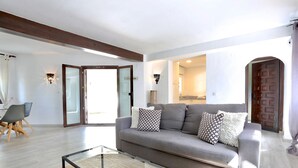 Ein modernes Wohnzimmer mit grauem Sofa, Glastisch und Essbereich mit Tisch und Stühlen.
