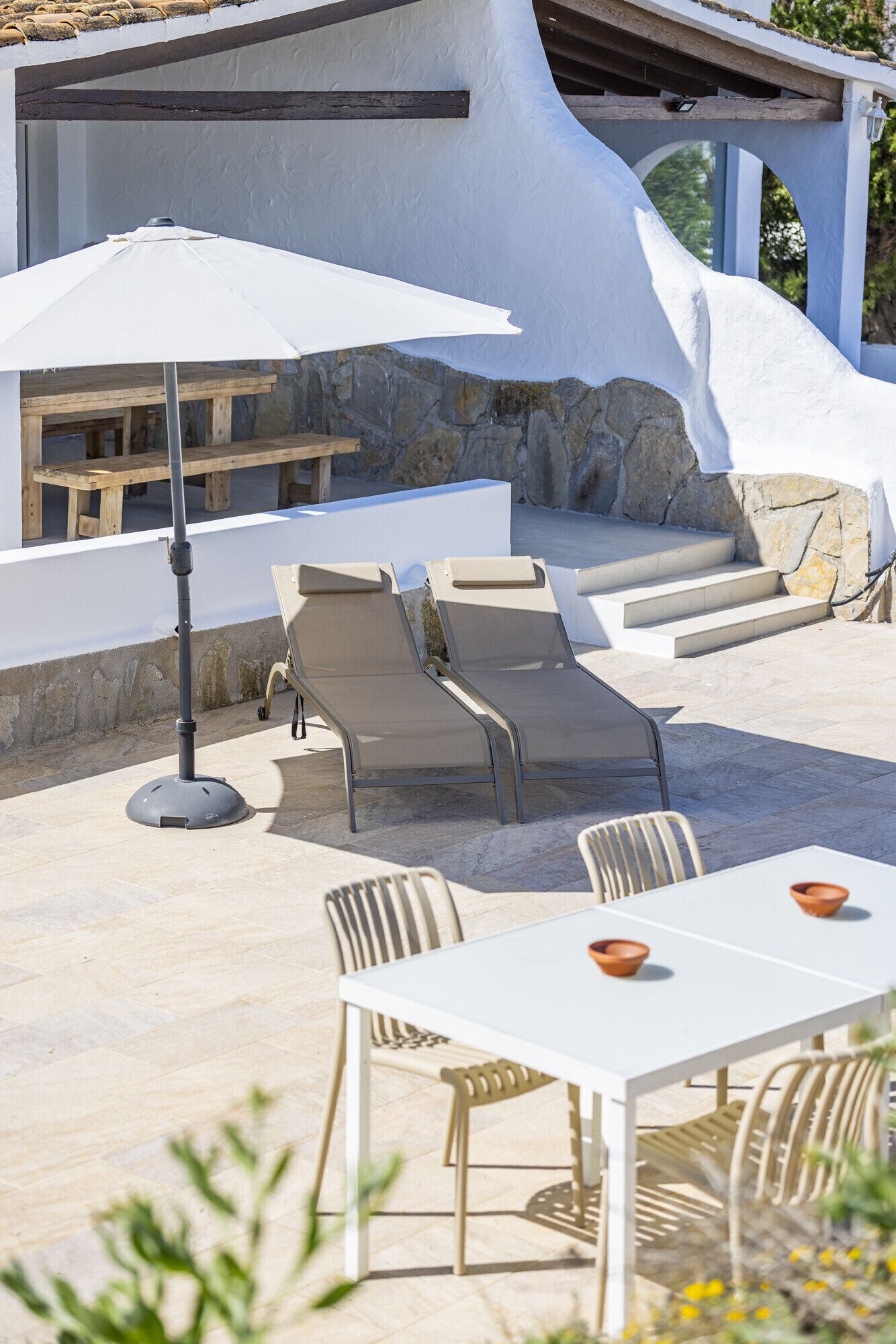 A sunlit outdoor seating area with lounge chairs, a table, and a pergola structure.