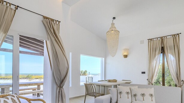 A modern living room with a sofa, two round tables, a wicker chair, and a view of the beach. - Villa LA LUNA 1ª Línea Playa (Denia)