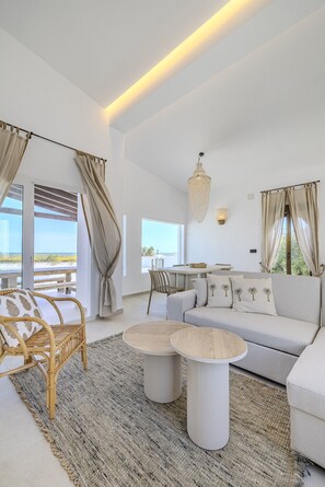 A modern living room with a sofa, two round tables, a wicker chair, and a view of the beach. - Villa LA LUNA 1ª Línea Playa (Denia)