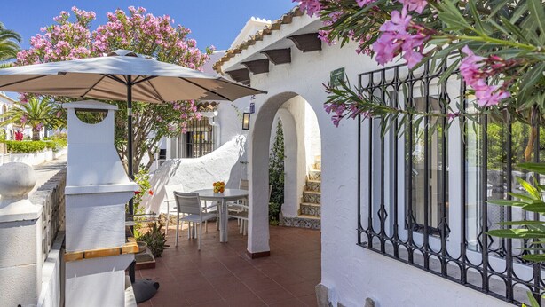 A patio area with a table and chairs, a white column, and pink flowers.