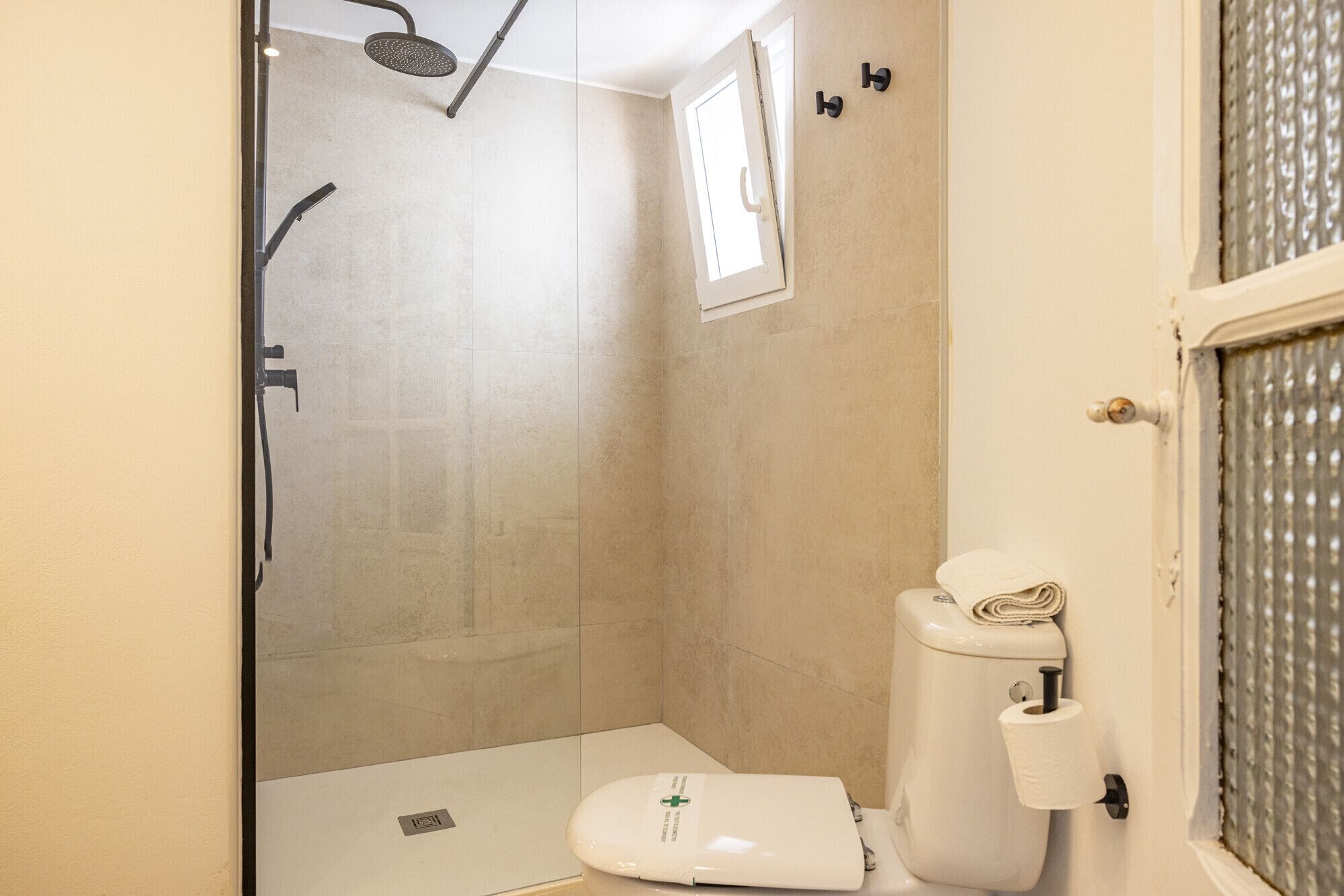 Een kleine, praktische badkamer met een douche, toilet en een raam.