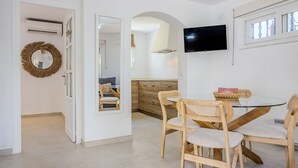A dining area with a round table, four wooden chairs, a television mounted on the wall, and a wicker basket on the table.