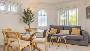 A modern living room with a grey sofa, wooden chairs, a glass table, and a potted plant.