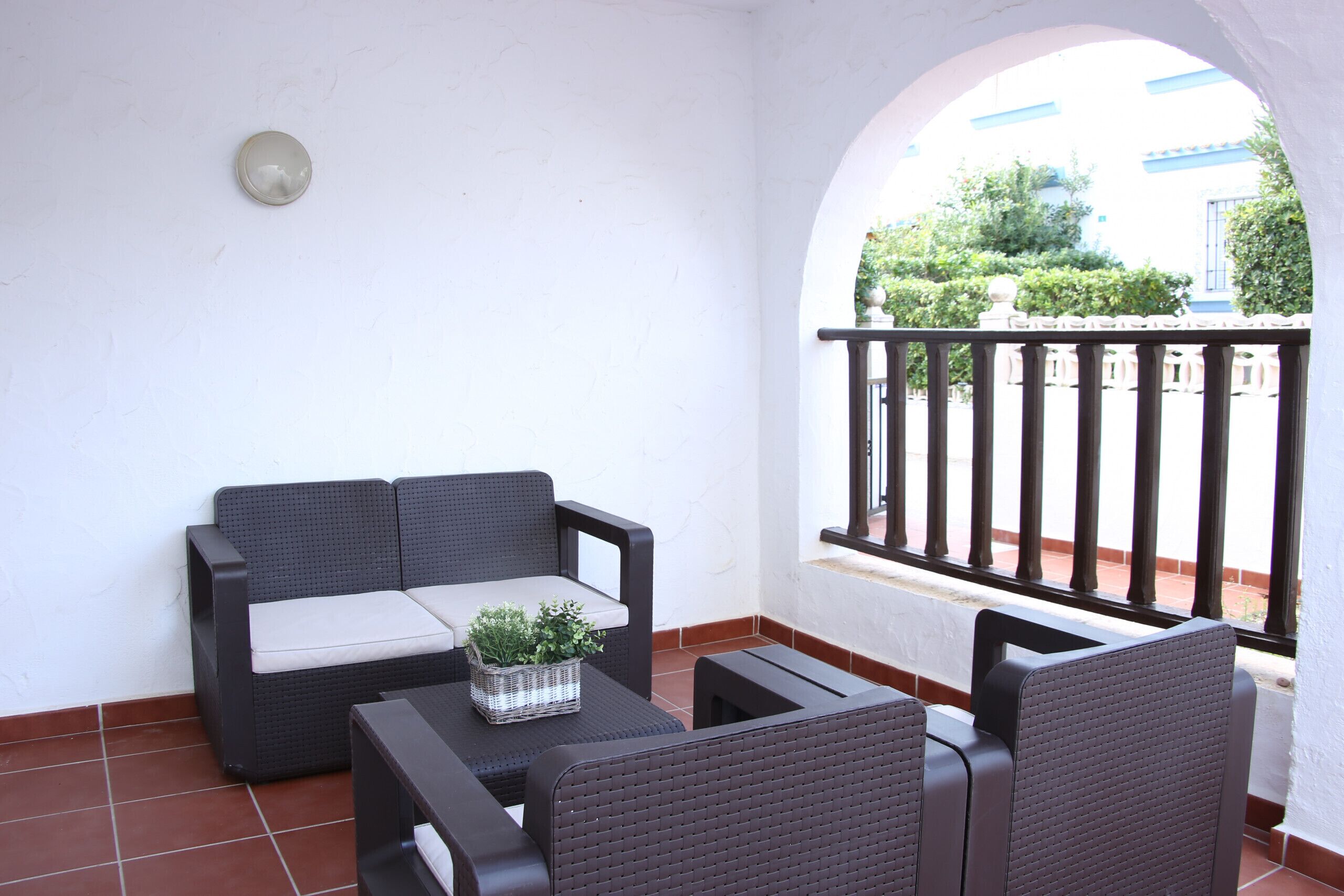 A patio with a black wicker sofa, a small table with a plant, and a black chair.