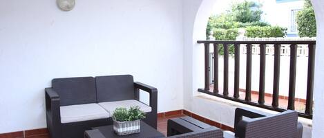 A patio with a black wicker sofa, a small table with a plant, and a black chair.