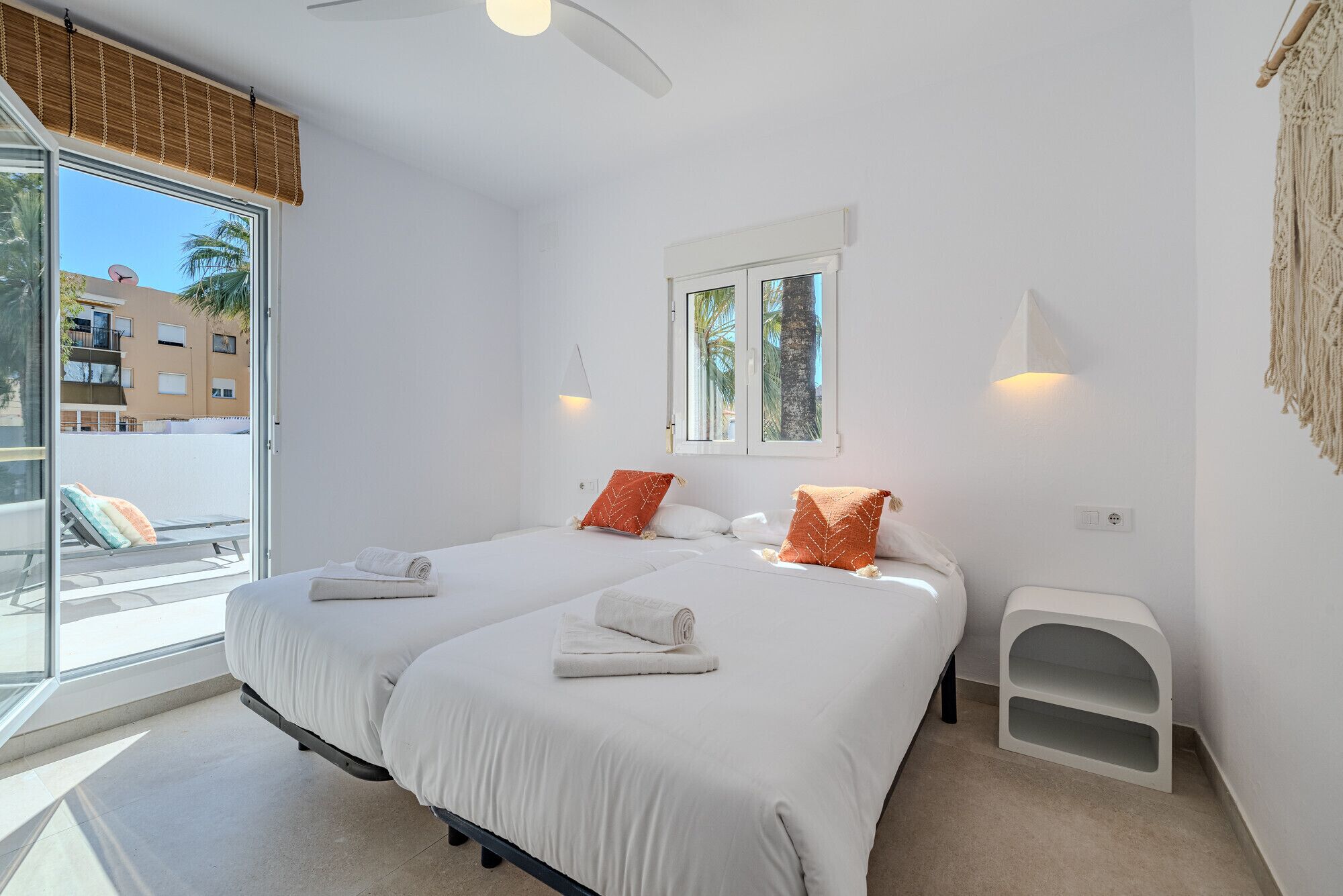 A modern hotel room with two beds, a window with a view of palm trees, and a balcony.