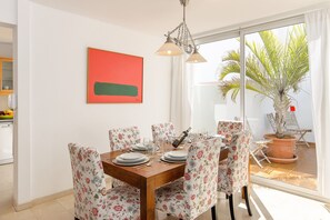 Un coin repas avec une table en bois, des chaises à motifs floraux, un tableau abstrait rouge et une plante en pot près de la fenêtre.