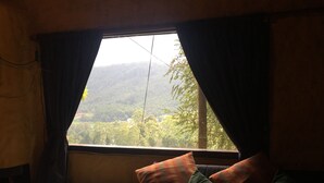 A room with a bed, a window with curtains, and a view of a forested landscape. - Misty Mountain Villas (Nuwara Eliya)
