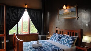 A bedroom with a wooden bed, a nightstand, a lamp, a window with curtains, and a wall-mounted picture. - Misty Mountain Villas (Nuwara Eliya)