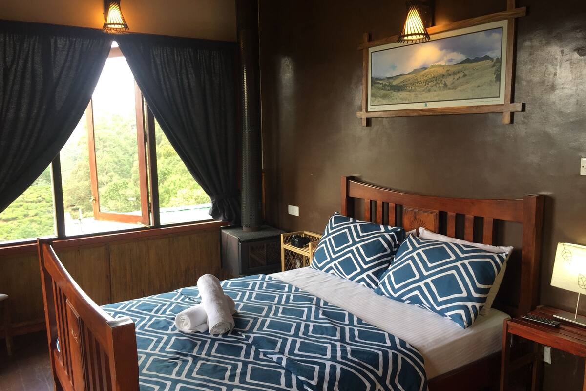Ein Schlafzimmer mit Bett, Nachttisch, Lampe, einem Gemälde und einem Fenster mit Vorhängen.