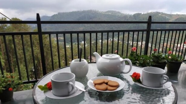 A table with a teapot, cups, saucers, and cookies on a balcony with a mountain view. - Misty Mountain Villas (Nuwara Eliya)
