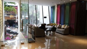 Um hall de hotel moderno com divisória de vidro, um sofá, uma mesa de centro e um vaso de flores.